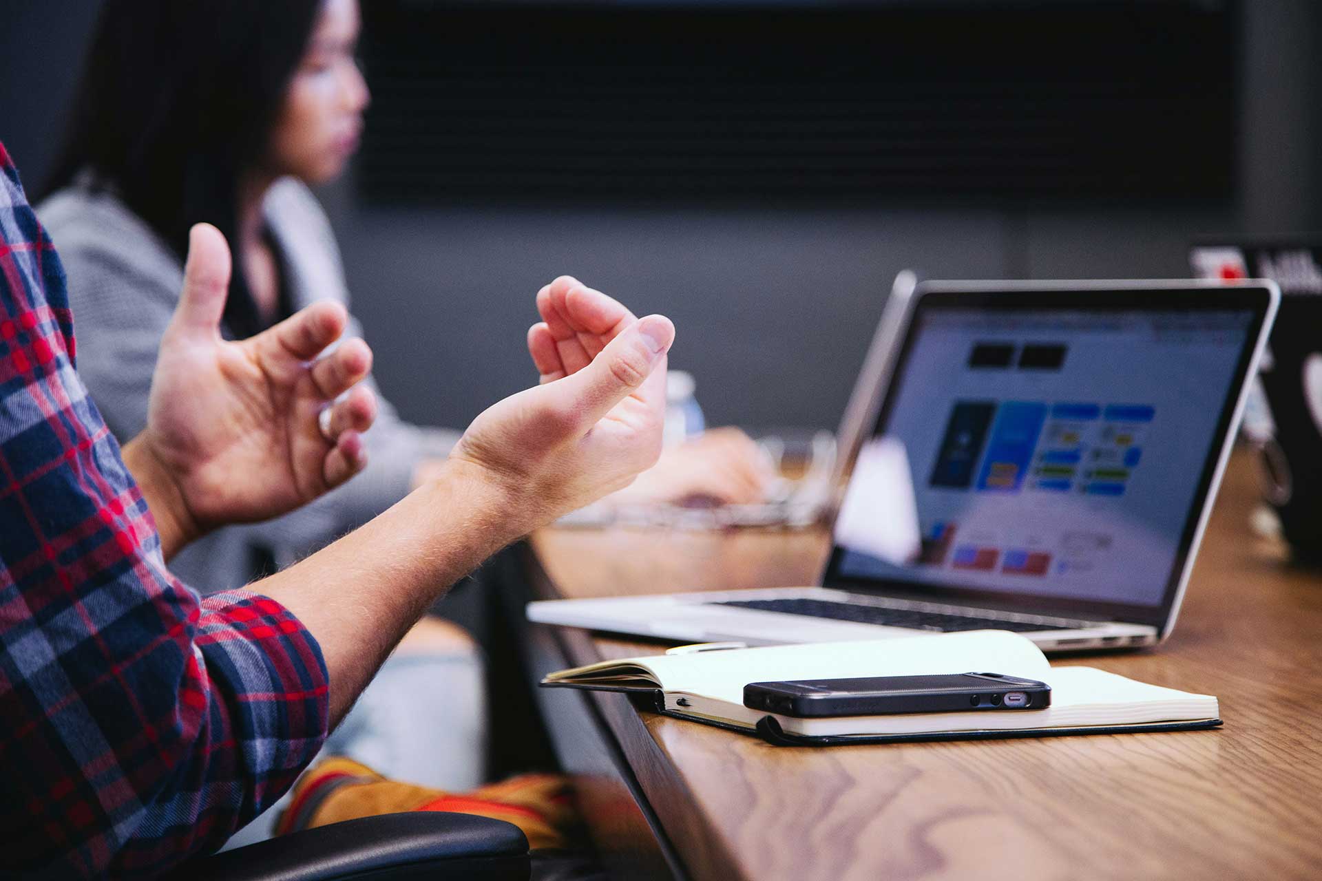 Close-up of hands gesturing during a meeting with a laptop showing interface designs.